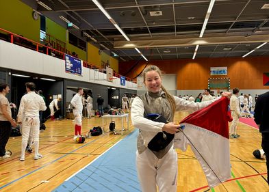 DHM Fechten 2024 Eine Person im Fechtanzug steht zentral in einer Sporthalle und präsentiert eine T-Shirt.