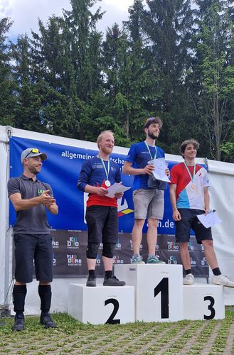 Preisverleihung der Deutschen Hochschulmeisterschaft im Mountainbike Enduro. Man sieht drei Studierende auf dem Treppchen bei der Preisverleihung mit einer Urkunde