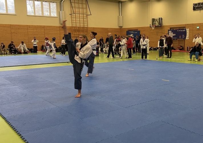 Man sieht eine Person auf einer Mattenfläche und weißer Kleidung, die Teakwondo macht.